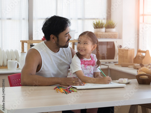 Asian young father with cute little daughter enjoying coloring in the kitchen. Home school, family acitivity on special day concept. photo