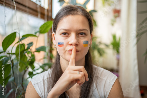A young Russian-Ukrainian girl with the flag of Ukraine and Russia on her face is showing keep silence. The concept of participation of the Ukrainian people in the war with Russia. Not war concept