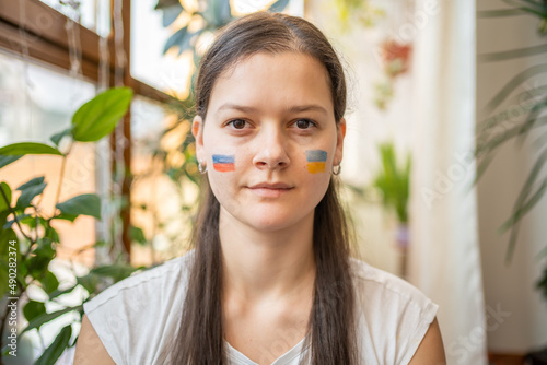 Portrait of young Russian-Ukrainian girl with the flag of Ukraine and Russia on her face. The concept of participation of the Ukrainian people in the war with Russia. Not war concept