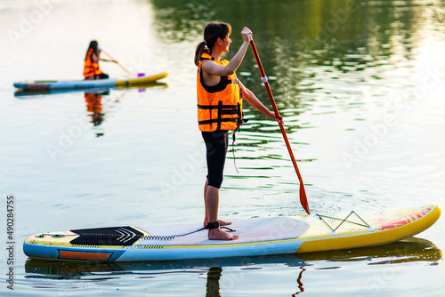 young woman in orange life jacket on supboard at river