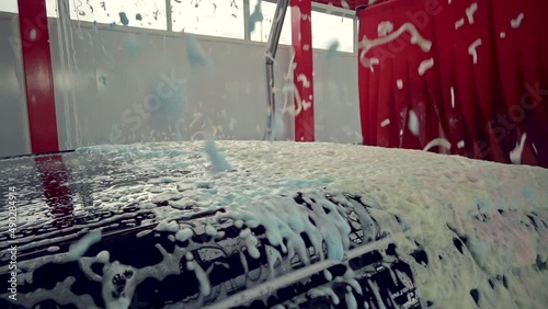 Black car moving though automatic car wash machine. Soap spray over the car. Slow motion shot