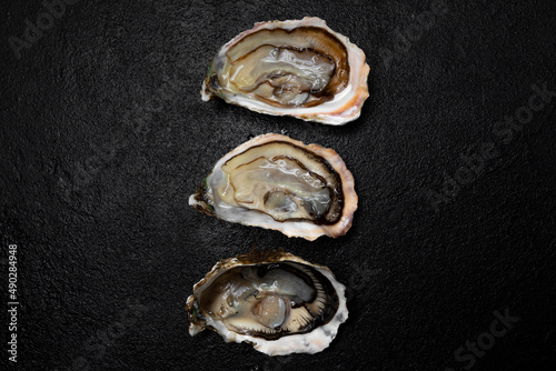 Sea delicacy fresh open oysters are laid out on a dark background.
