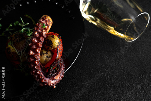 Sea delicacy grilled octopus with grilled vegetables. Dishes on a dark decorated background with a glass of wine