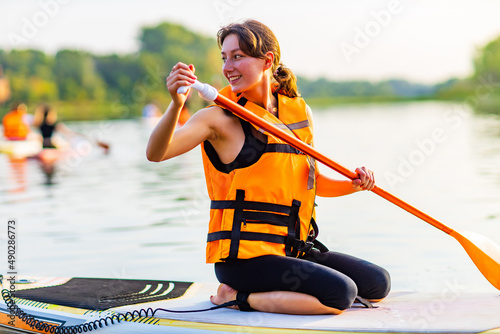 young woman in orange life jacket on supboard at river
