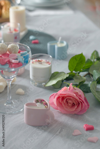Peony pink rose with wax hearts, heart-shaped candle on the background of other candles on the table.