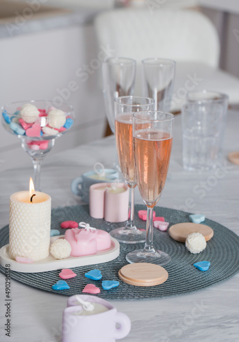 Wax hearts on the table against the background of candles, flowers, champagne glasses.