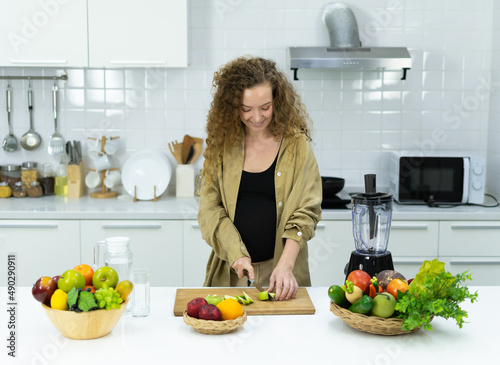 woman smile  stand  cut green apple  make diet fruit juice  looking at knife in kitchen with copy space. beautiful caucasian pregnant woman cooking healthy diet fruit or food in kitchen