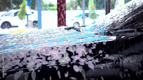 Black car moving though automatic car wash machine. Soap spray over the car. Slow motion shot