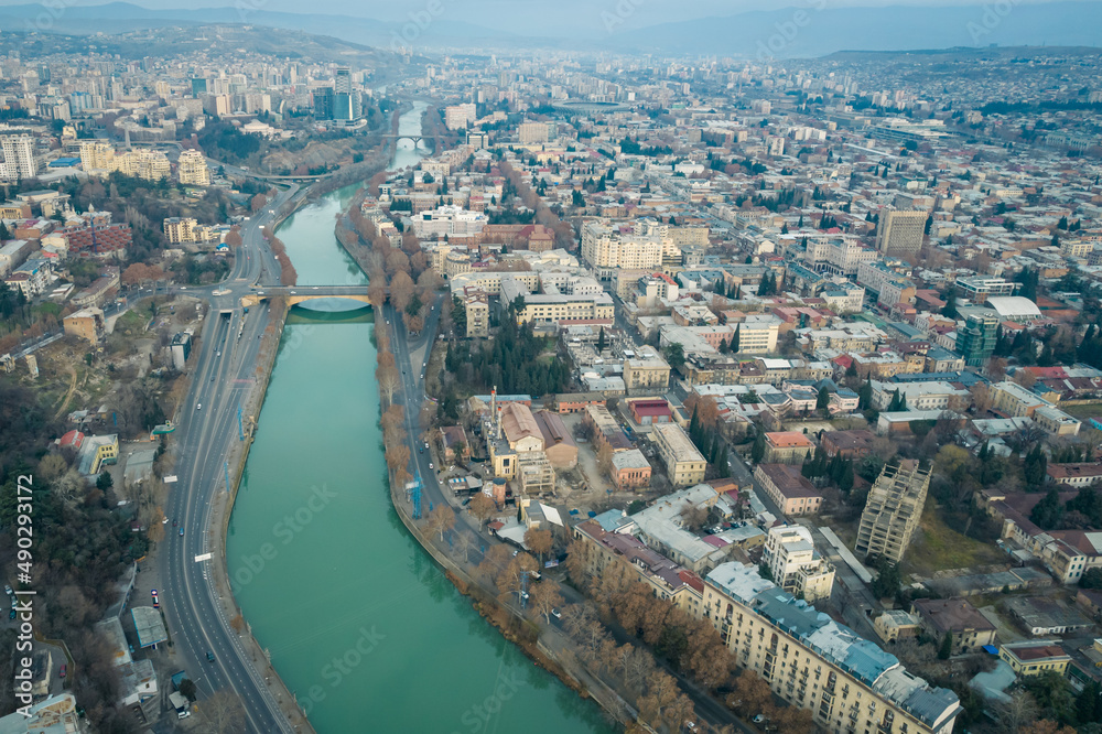 Aerial view of Tbilisi city center with churches and modern buildings and emerald waters of Kura river
