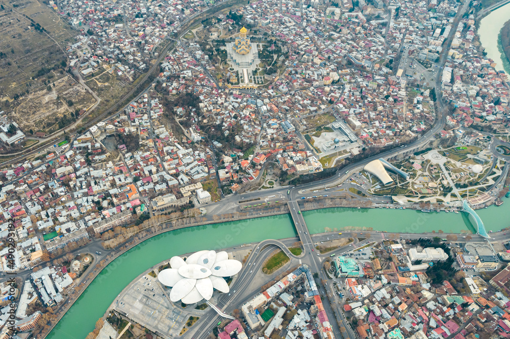 Fototapeta premium Aerial view of Tbilisi city center with churches and modern buildings and emerald waters of Kura river