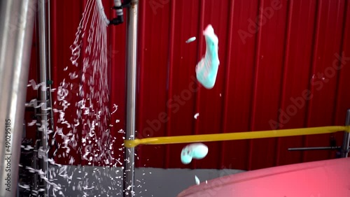 White car moving though automatic car wash machine. Soap spray to clean the car. Slow motion shot