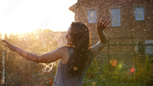 Happy smiling woman is under the rain. Stunning golden sun rays shine on playful young woman enjoying a summer rain. slow motion