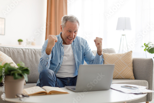 Mature man using laptop celebrating success shaking fists screaming yes