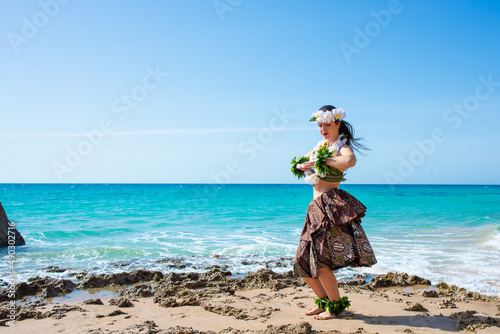 Hawaiian woman enjoys hula dancing on the beach barefoot wearing traditional costume