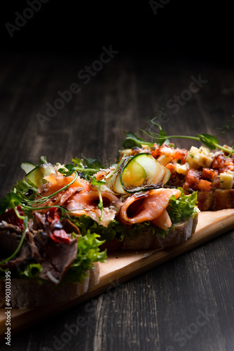 a dish of 3 different tapas stuffed with meat, fish and various microgreens, served on a board against a dark background