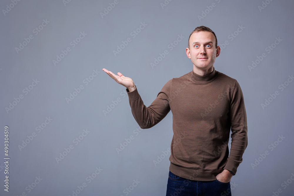 Fototapeta premium Portrait of cheerful young man smiling while looking at camera pointing with finger on gray background.