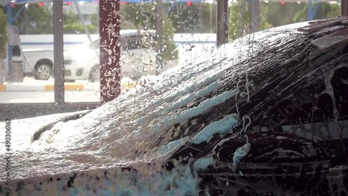 Black car moving though automatic car wash machine. Soap spray on to clean the car. Slow motion shot