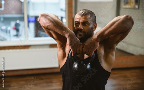 Close up portrait of African American muscular man lifting a kettlebell at gym.