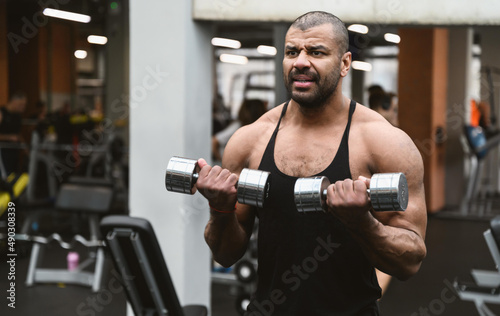 Muscular afro-american man working out in gym doing exercises with dumbbells at shoulders without coach or instructor. Fitness crossfit bodybuilding concept © ANR Production