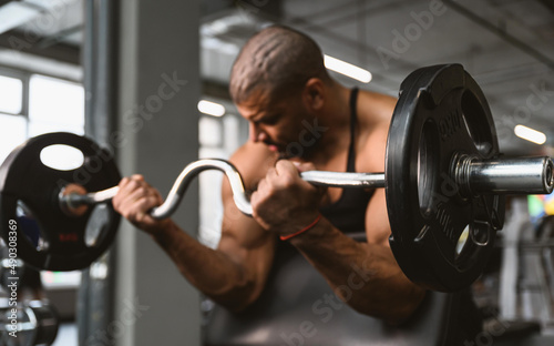 An afro american male bodybuilder performs a biceps exercise in a sports club. The athlete is preparing for the competition.
