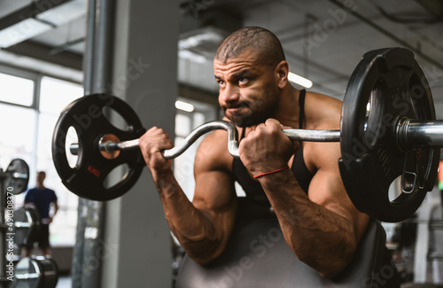 An afro american male bodybuilder performs a biceps exercise in a sports club. The athlete is preparing for the competition.