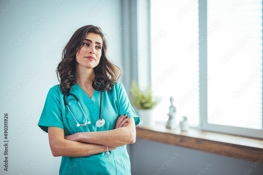 Female nurse wearing green scrubs, arms crossed. Medical professional working in hospital. Attractive female doctor at work. Smiling female nurse in medical scrubs Female nurse wearing green scrubs, arms crossed. Medical professional working in hospital. Attractive female doctor at work. Smiling female nurse in medical scrubs