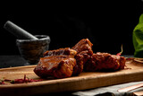 fried ribs in sauce served on a board, on a dark background