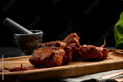fried ribs in sauce served on a board, on a dark background