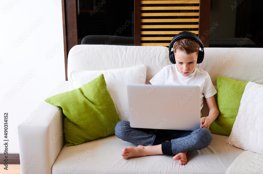 Concentrated schoolboy wearing headphones with laptop play online games at home. Distance learning in quarantine Concentrated schoolboy wearing headphones with laptop play online games at home. Distance learning in quarantine