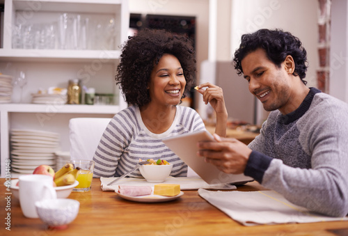 The day is better when we start it together. Shot of a happy couple enjoying breakfast together while looking a digital tablet.