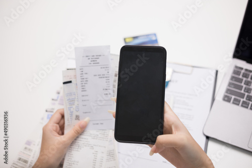 Close up woman is using a smartphone to scan the bill to calculate her income and expenses. In hand there were bills to pay a lot in debt. Purchase with scan qr code payment online.