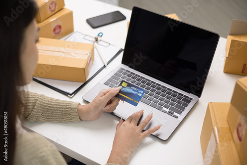 Shopping online. Young asian woman input the serial number of credit card to laptop for shopping payment. Buy item online delivery at home. Small business entrepreneur with many parcel box on table