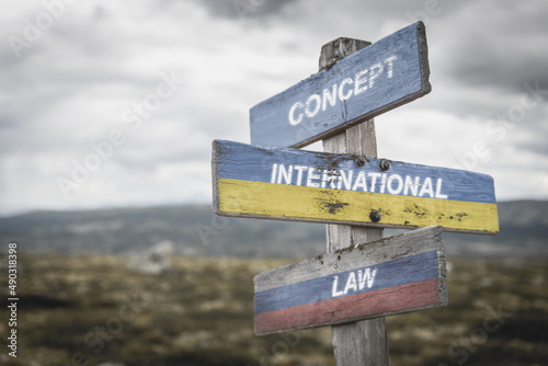 concept international law text quote on wooden signpost outdoors on nato colored flag, ukrainian flag and russian flag.