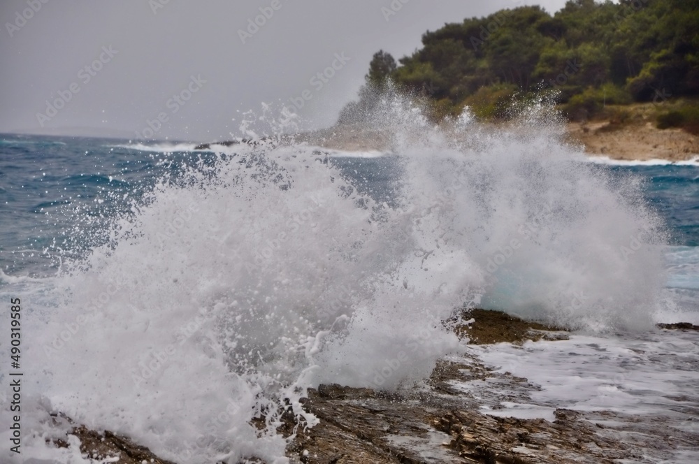 Waves crashing on rocks. Waves breaking on the shore of Big Beach. Background, coastline.Wave rolling on the coast of island Losinj with horizon line in background.