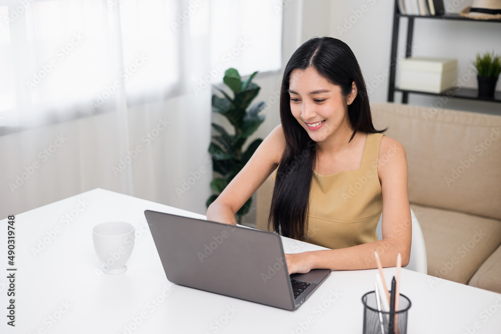 Young asian beautiful business woman working with laptop sitting at home. Smiling charming happy young female doing homework meeting conference with team at home. Young asian beautiful business woman working with laptop sitting at home. Smiling charming happy young female doing homework meeting conference with team at home.