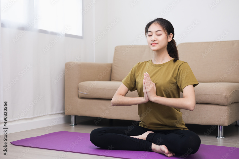 Young asian sport woman sitting on the yoga mat practicing meditation. Fitness or exercise at home. Beautiful female relaxing after workout.