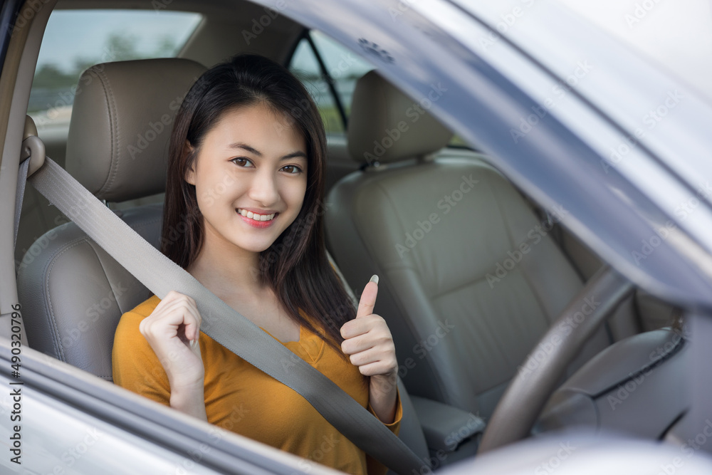 Young beautiful asian women getting new car with safety belt. she very happy and excited. she sit and put on seatbelt. Smiling female driving vehicle on the road. showing thumb up