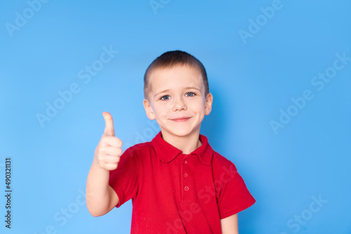 charming little smiling boy in a red shirt shows thumbs up, on a blue background