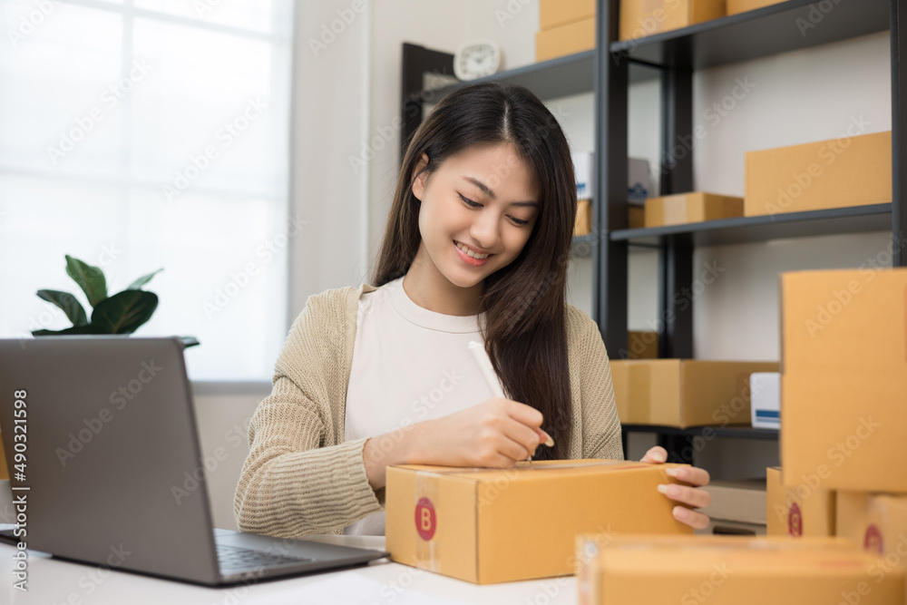 Young asian business woman writing address to sending product to customer. Online business working at home. Startup Small business owner entrepreneur Young asian business woman writing address to sending product to customer. Online business working at home. Startup Small business owner entrepreneur
