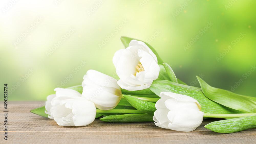 white tulips lying on a wooden table on a blurred natural background