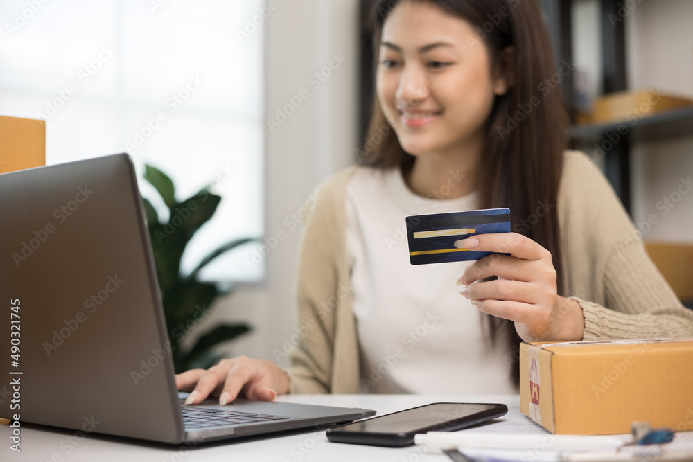Shopping online. Young asian woman input the serial number of credit card to laptop for shopping payment. Buy item online delivery at home. Small business entrepreneur with many parcel box on table Shopping online. Young asian woman input the serial number of credit card to laptop for shopping payment. Buy item online delivery at home. Small business entrepreneur with many parcel box on table