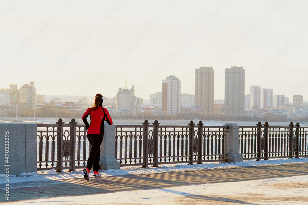 Sport, fitness inspiration and motivation. A young woman runs along the embankment promenade in the snow, a winter day. Across the river in blur, the Chinese city of Heihe. Sports concept Sport, fitness inspiration and motivation. A young woman runs along the embankment promenade in the snow, a winter day. Across the river in blur, the Chinese city of Heihe. Sports concept