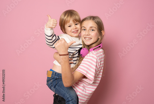 Little brother and sister together in casual clothes showing thumbs up standing isolated over pink background. Lifestyle concept.