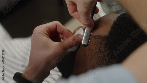 The barber shaves the contour of the temple of a man with a dangerous razor