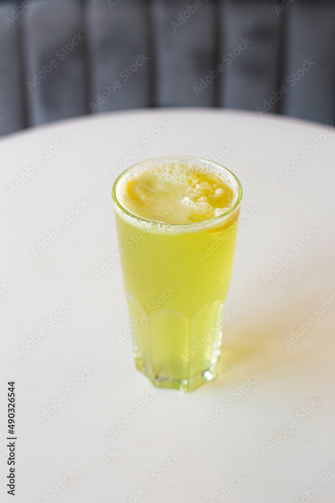 green lemonade with lemon in a glass glass on a white table with a blurred gray background. green lemonade with lemon in a glass glass on a white table with a blurred gray background.