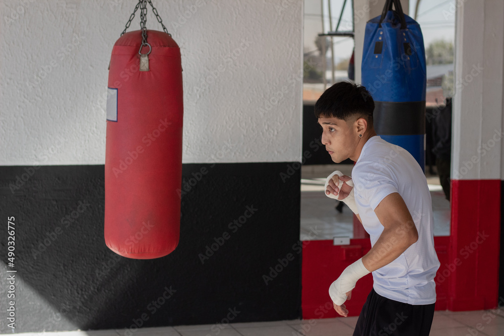 young latin boxer training only his fighting moves in the boxing gym, he wears a white sport shirt and white bandages on his hands.