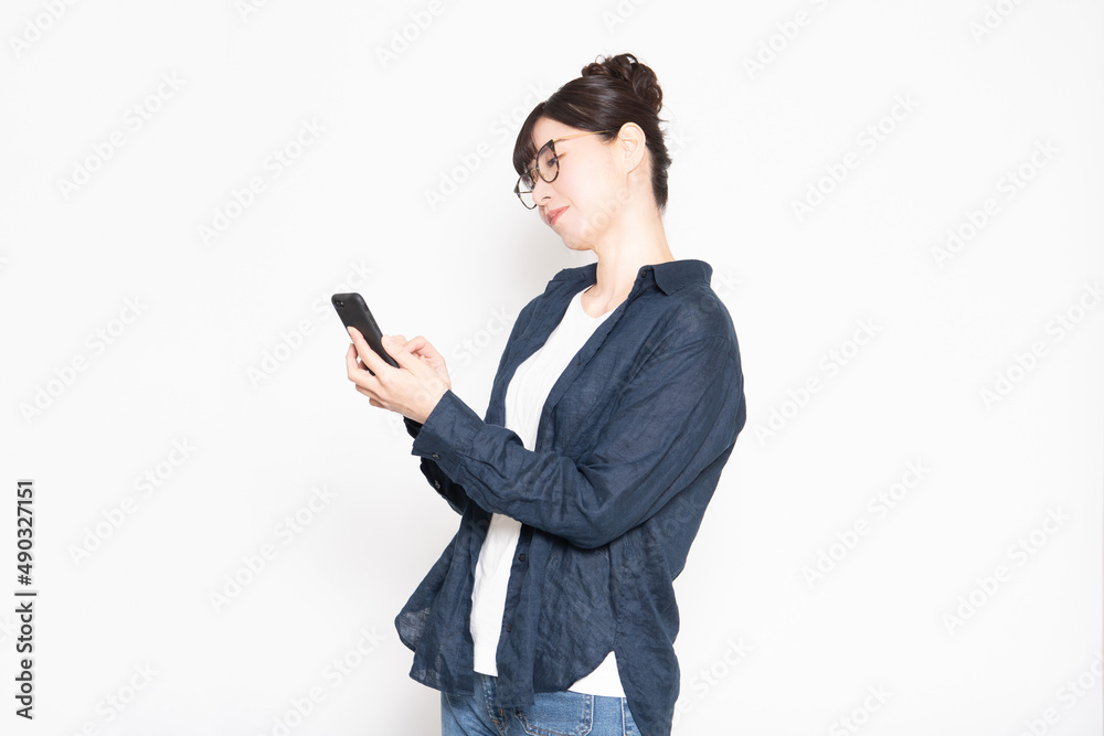 白い背景の前に立ってスマホを操作する眼鏡をかけた女性 白い背景の前に立ってスマホを操作する眼鏡をかけた女性