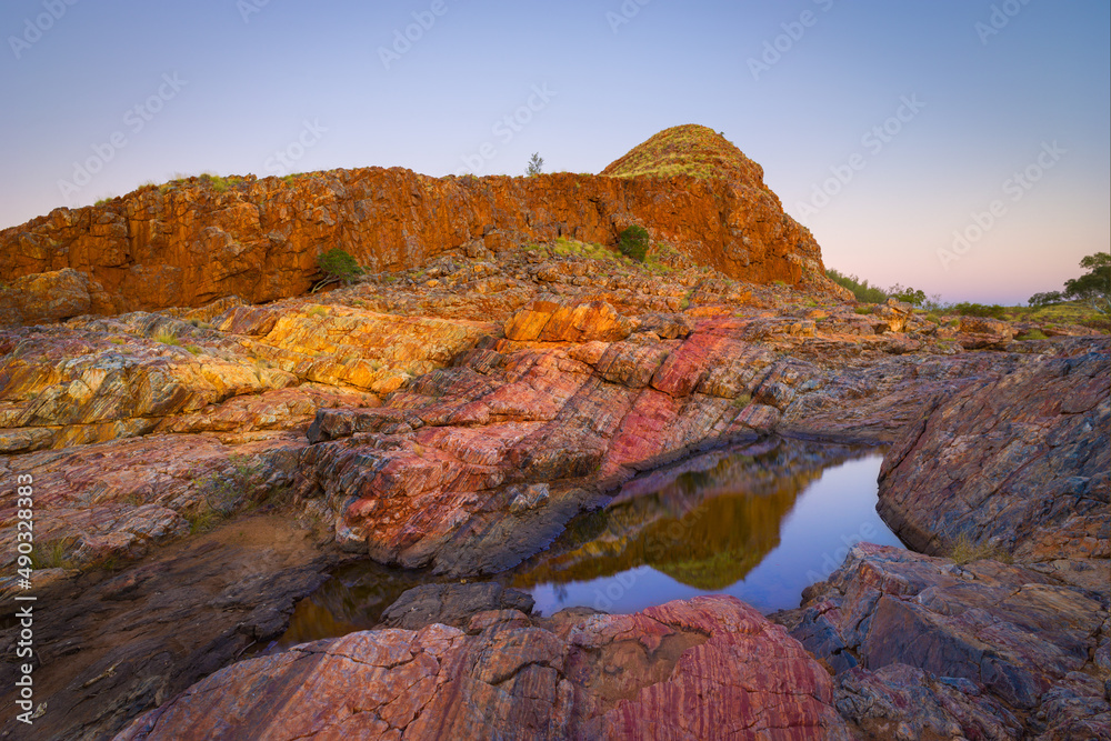 Colorful landscape at dawn with rocks consisting of red layers of Jasper and little pond in the vicinity of the village of Marble Bar, Western Australia