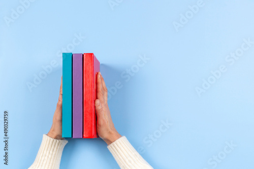 Female hands holding pile of books over light blue background. Education, self-learning, hobby, relax time at home