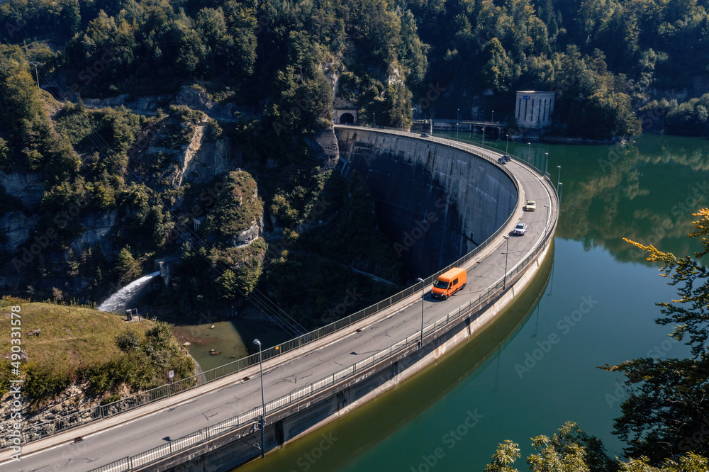 Aerial view of the Barrage de Rossens, a dam in the canton of Fribourg, Switzerland. Six vehicles are passing on the road that runs along the dam. Photograph taken in early fall.